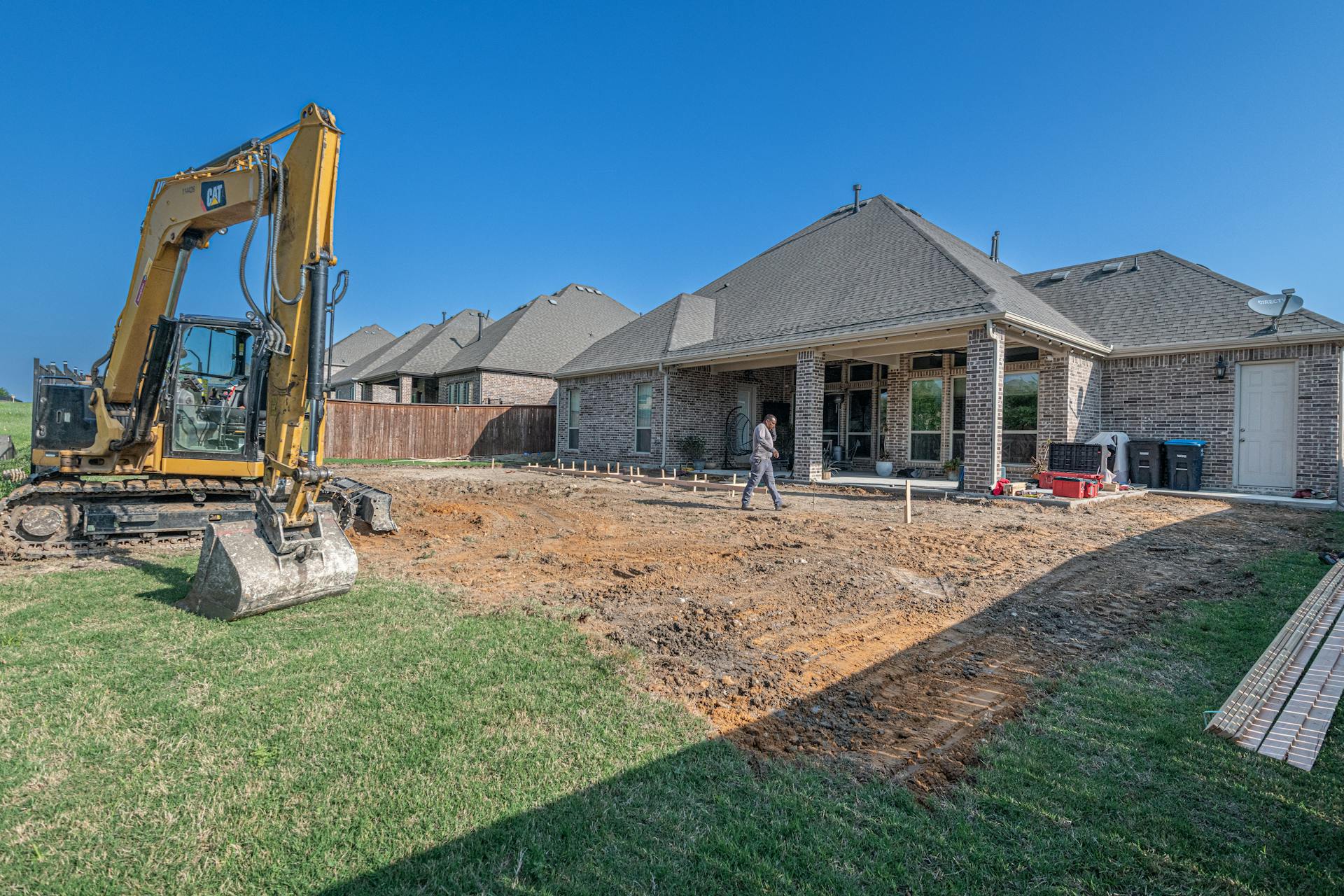 Contractor grading and leveling bare soil in a suburban backyard before sod installation