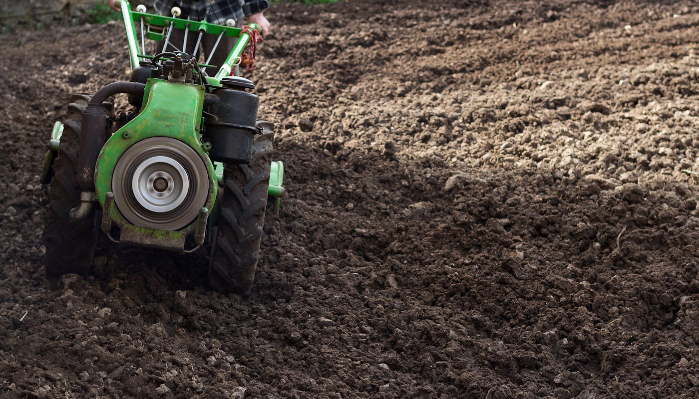 Farmer using small tractor cultivating and tilling soil in field before planting